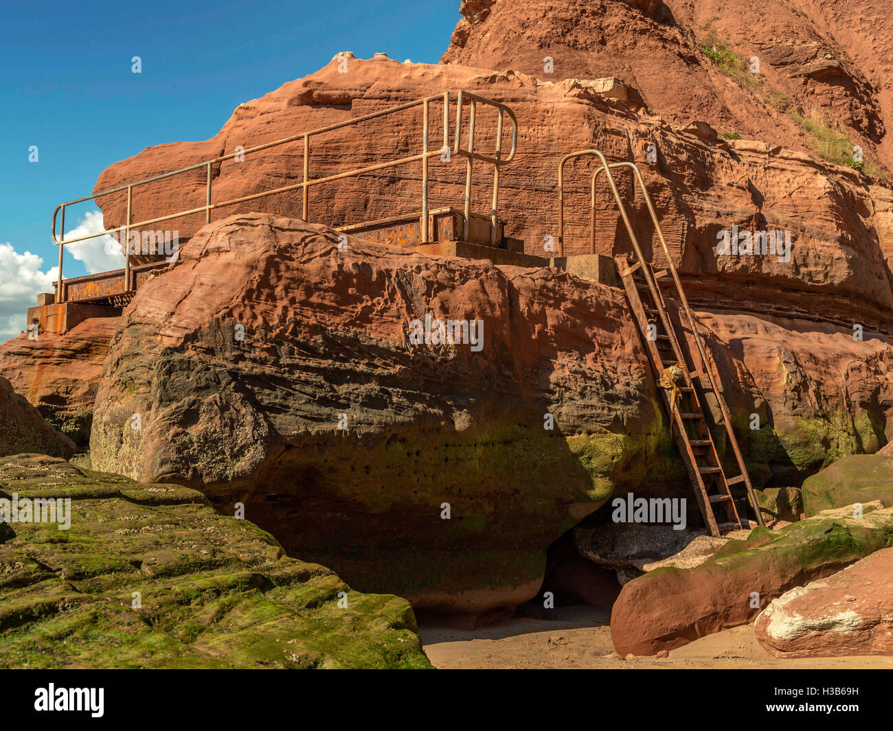 Rustic rock formations visible at low tide and rusting metal gangways at Orcome Point near the seaside town of Exmouth, Devon. Stock Photo
