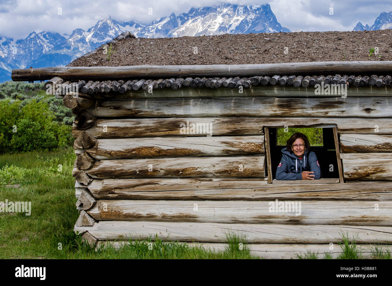 Woman in window of historic Cunningham Log Cabin Grand Teton National Park, Wyoming, USA. (MR) Stock Photo
