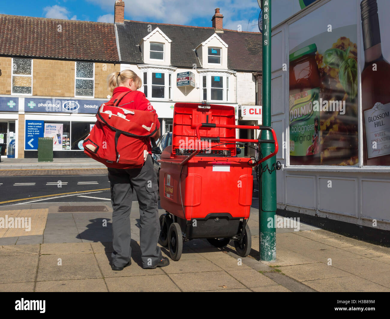 Post woman with her trolley safely locked taking out a bag of mail  for street delivery Stock Photo