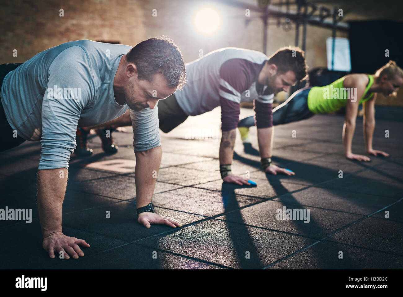Group of adults performing push up exercise drills at indoor physical fitness cross-training exercise facility with bright light Stock Photo