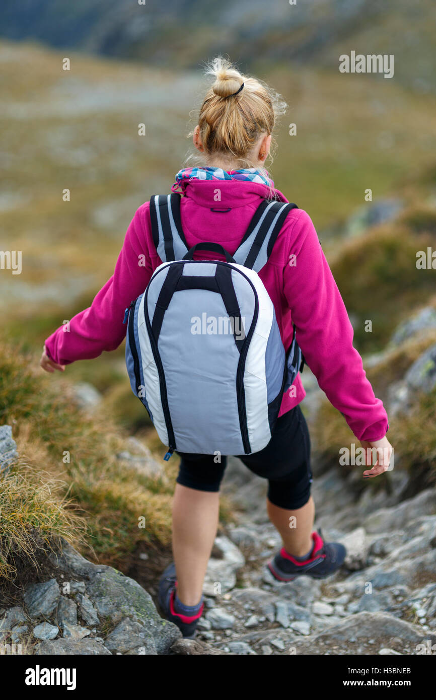 Young woman hiker with backpack walking a trail in rocky mountains ...