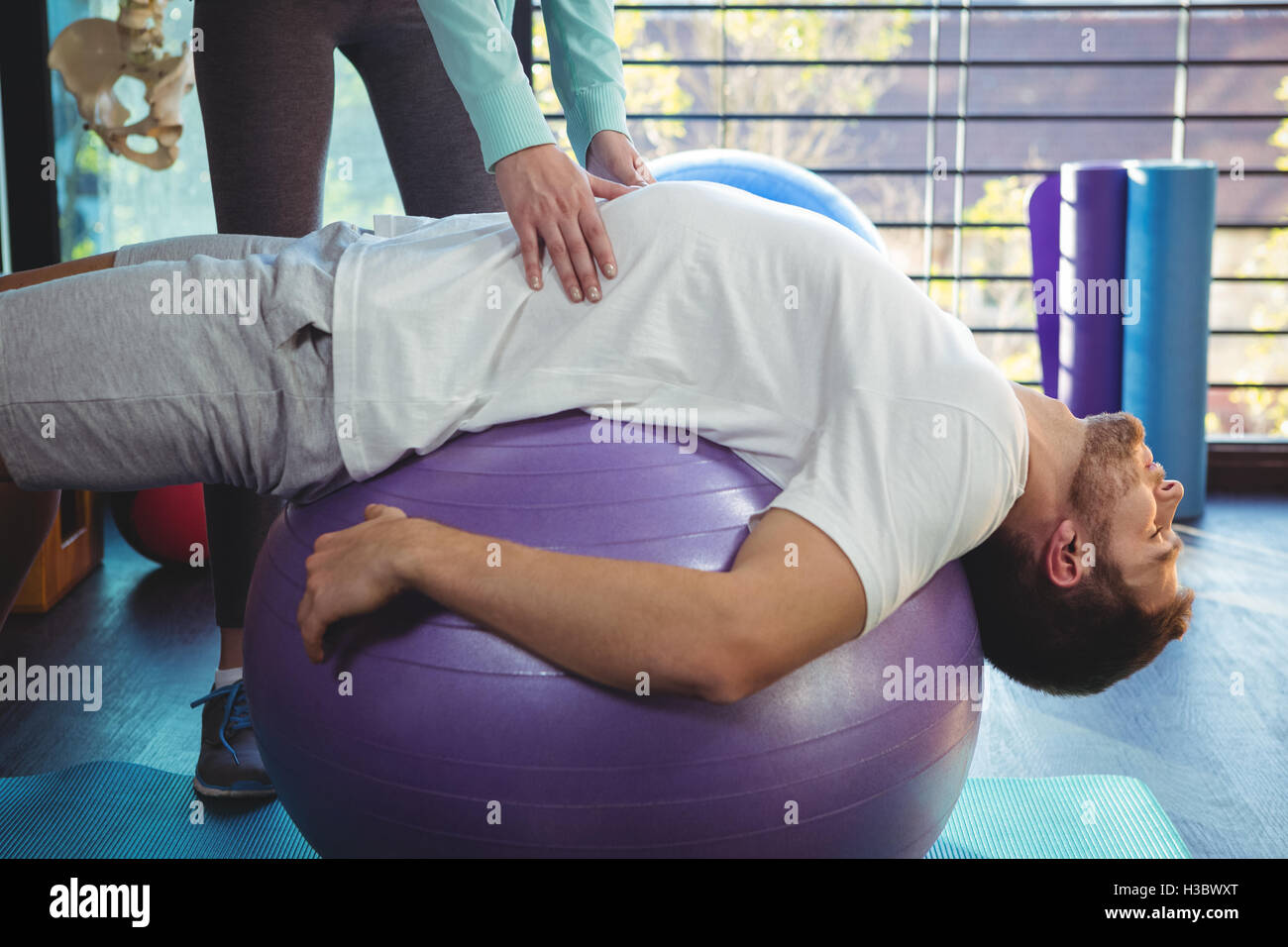 Female physiotherapist helping male patient on exercise ball Stock Photo