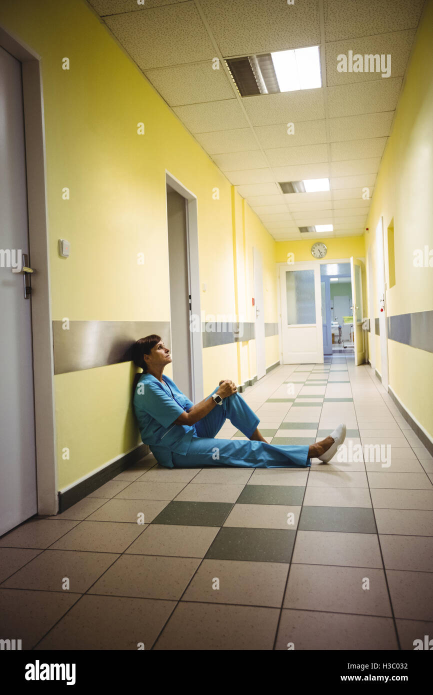 Depressed nurse sitting in corridor Stock Photo