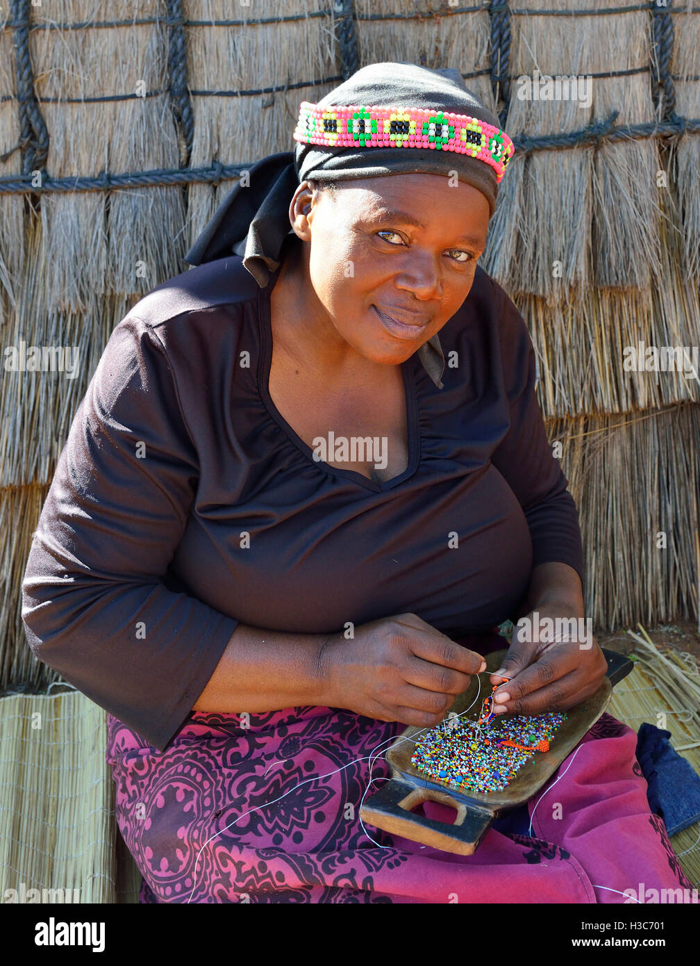 Zulu woman troupe member in traditional clothes making bead souvenirs in front a Zulu rondavel ,Shakaland Cultural Village,KwaZulu-Natal,South Africa Stock Photo