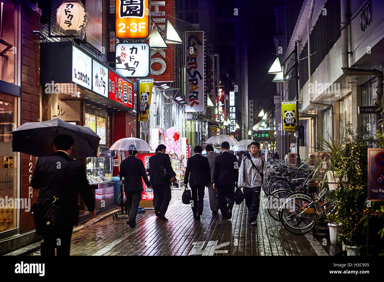 Night street after rain with beautiful light of cafe and shopes Tokyo area of Ueno station People walk under umbrellas. Stock Photo