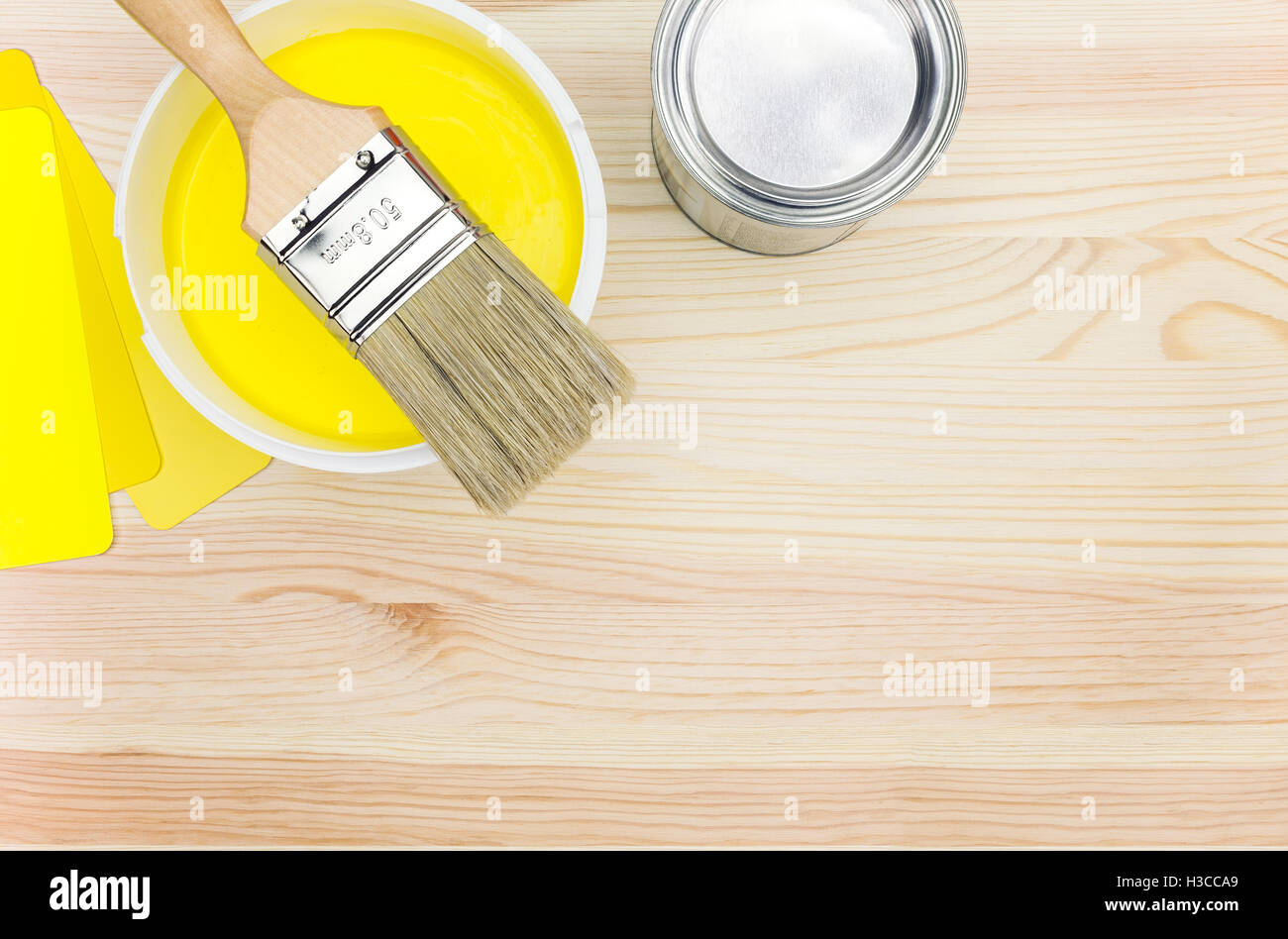 opened can of yellow paint and brush with color guide on white