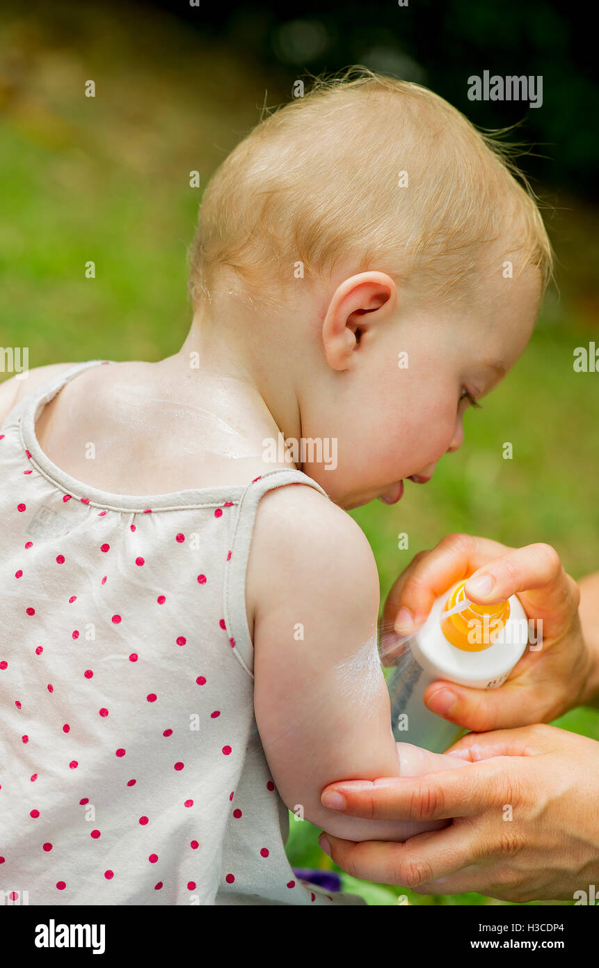 Parent spraying sunscreen on baby's arm Stock Photo