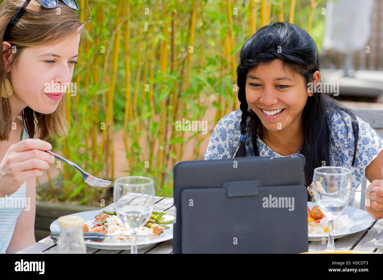 Women watching digital tablet while eating outdoors Stock Photo