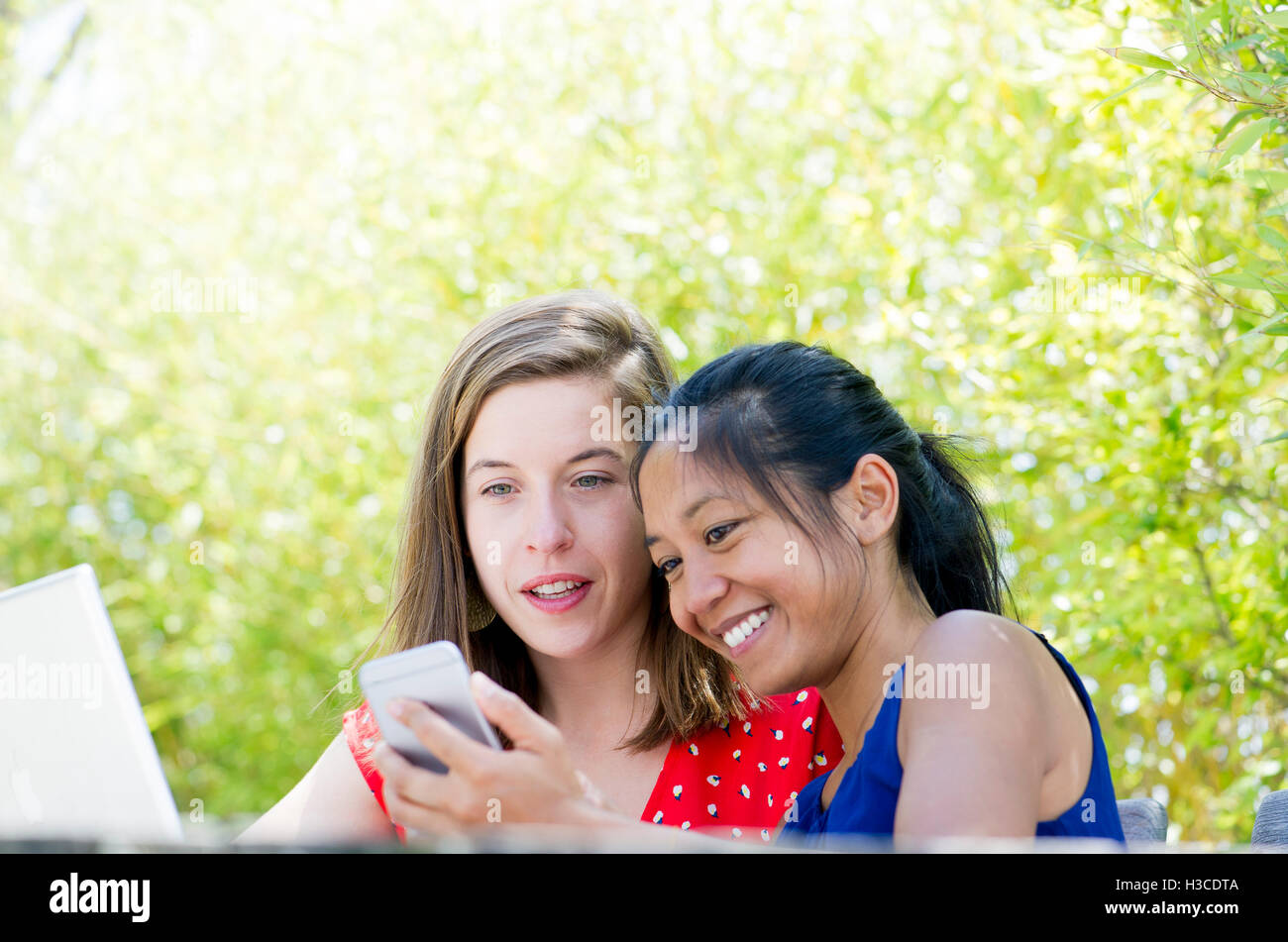 Women looking at smartphone together outdoors Stock Photo