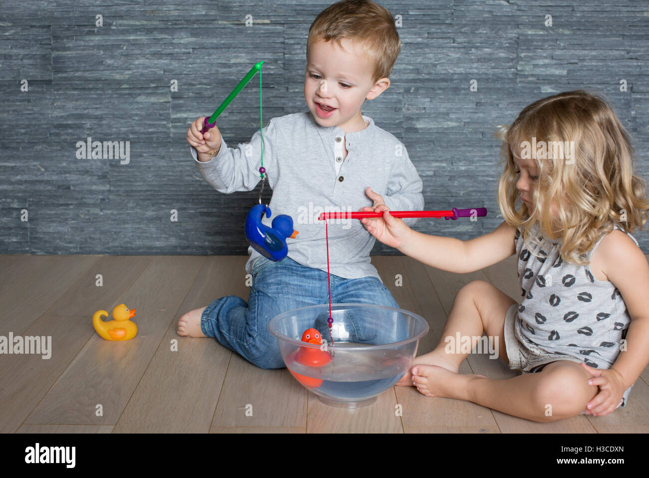 Children using toy fishing rods to catch rubber ducks floating in large bowl Stock Photo