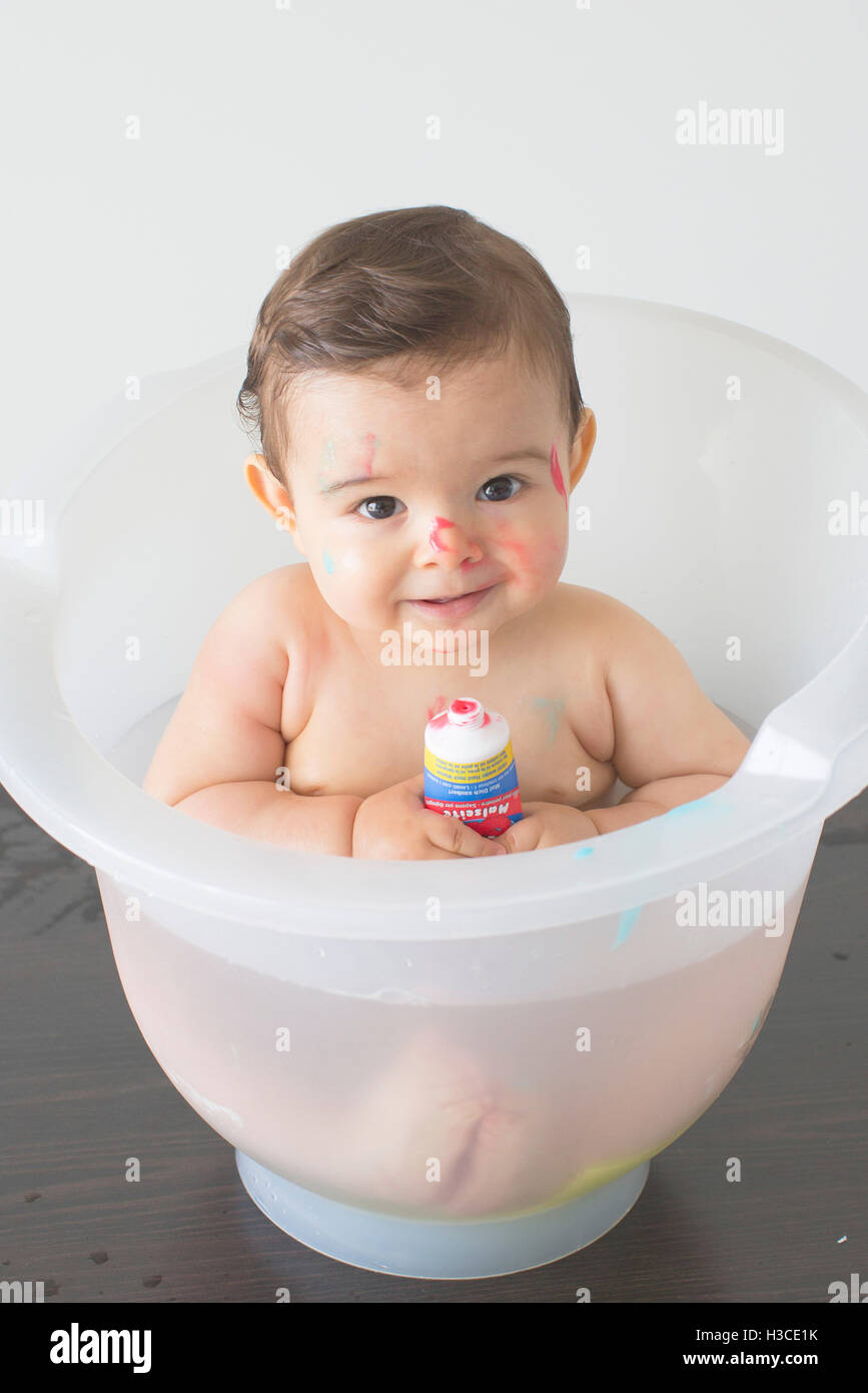 Happy little black baby girl sitting in bath tub playing with toys in  bathroom. Portrait of