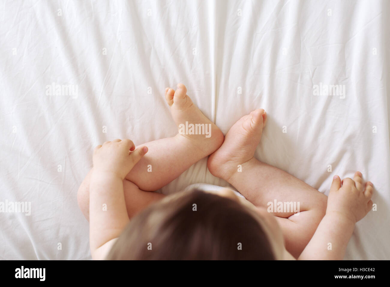 Baby sitting on bed, overhead view Stock Photo