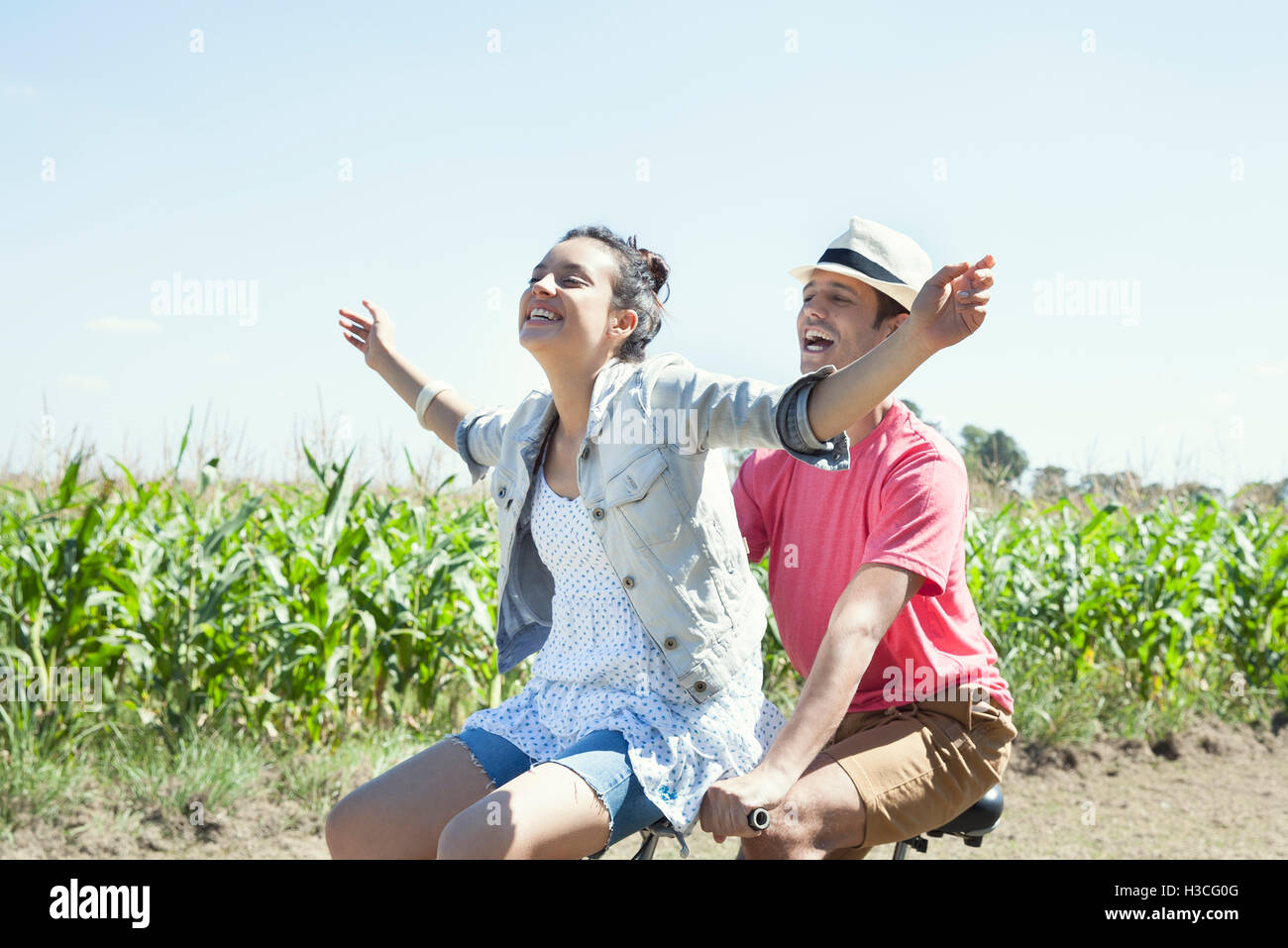 Couple riding bike together, woman with arms outstretched Stock Photo