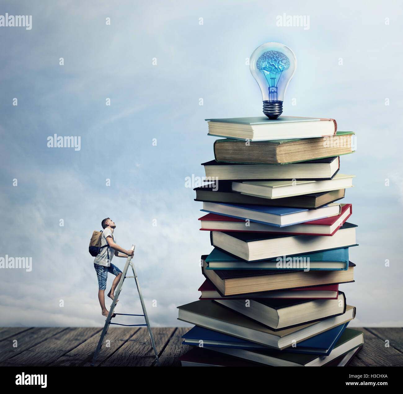 Young boy on the ladder, with a bag on his back, trying to climb a pile of books looking for a lightbulb. In search of knowlegde Stock Photo