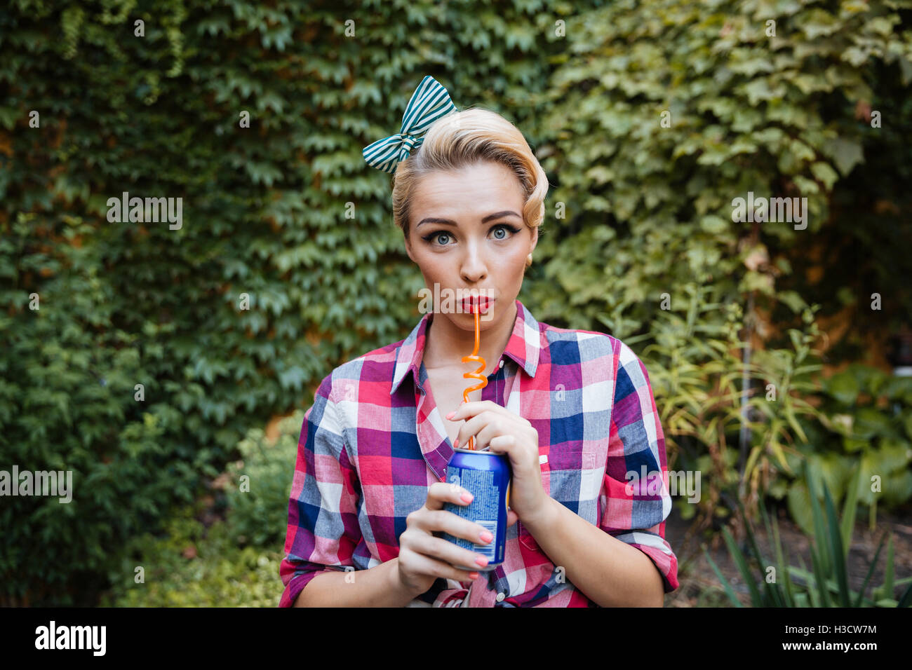 Cute playful pin-up girl drinking soda in the garden in summer Stock Photo