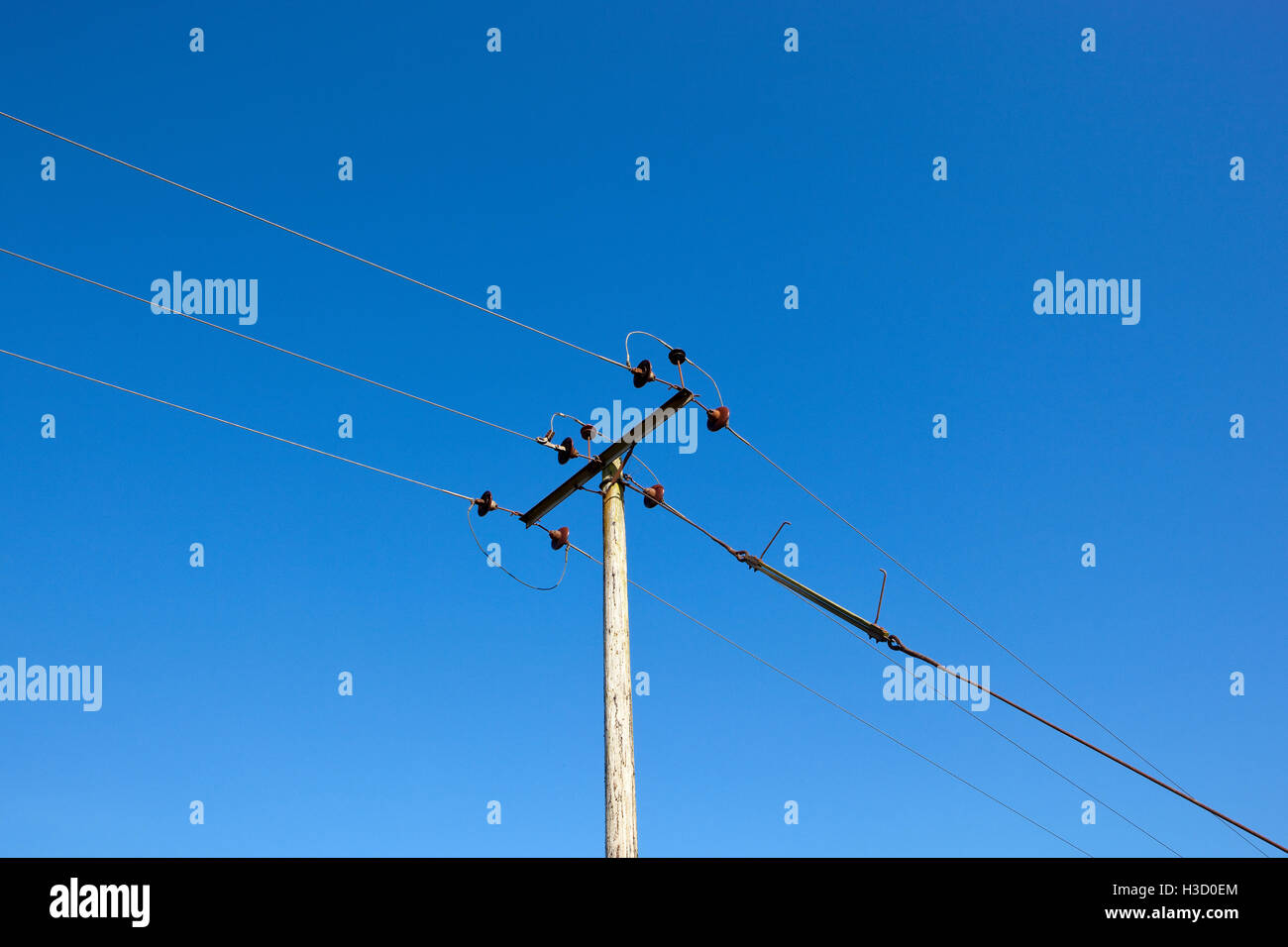 A wooden telegraph pole with wires on a clear blue sky background. Stock Photo