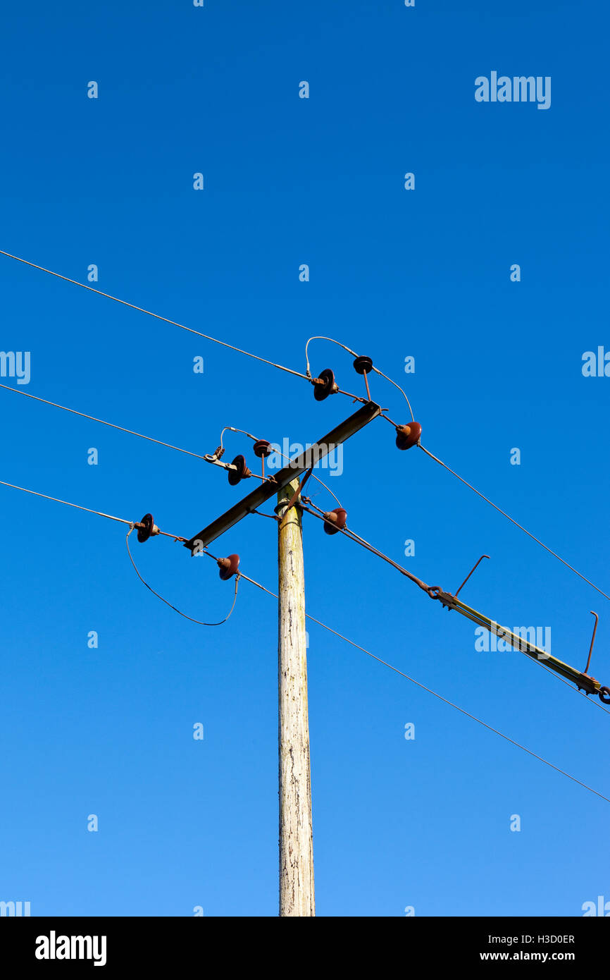 Detail of a wooden telegraph pole and wires with ceramic insulators on a clear blue sky background. Stock Photo
