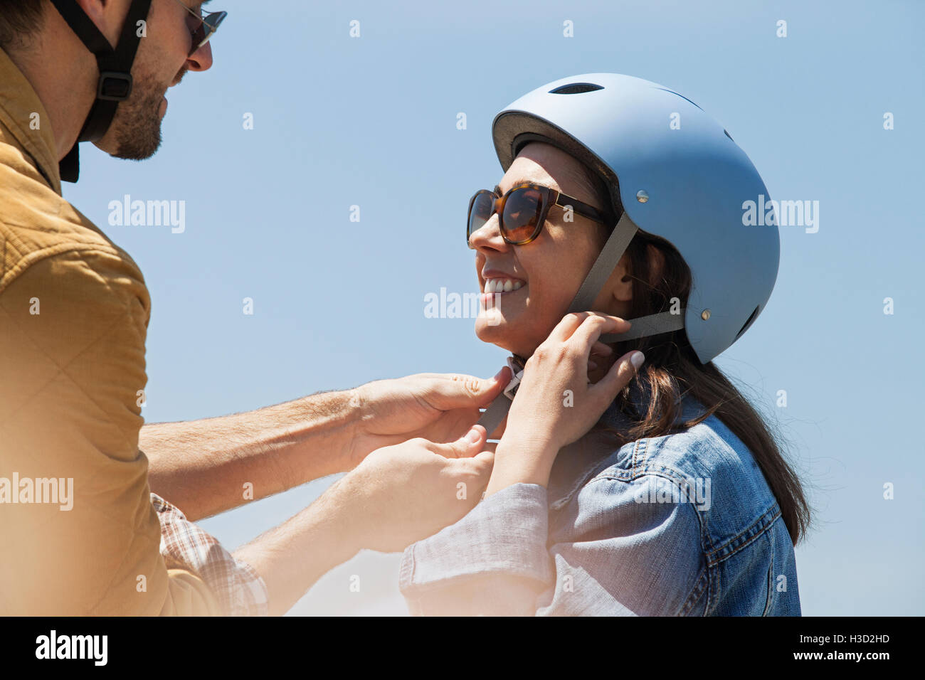 Man assisting woman in wearing bicycle helmet against clear sky on sunny day Stock Photo