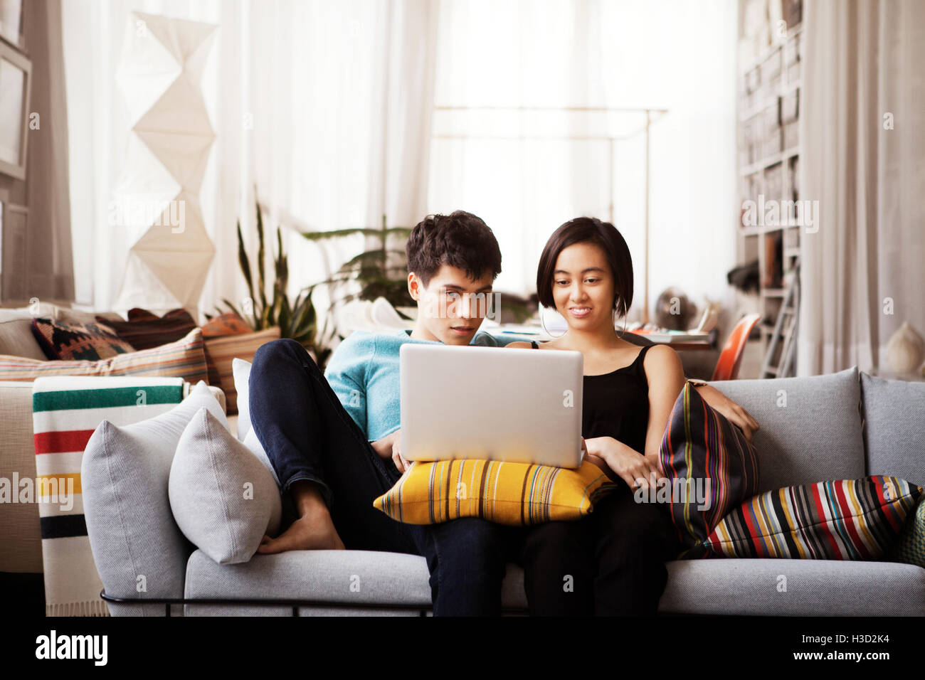 Young couple using laptop while sitting on sofa at home Stock Photo - Alamy