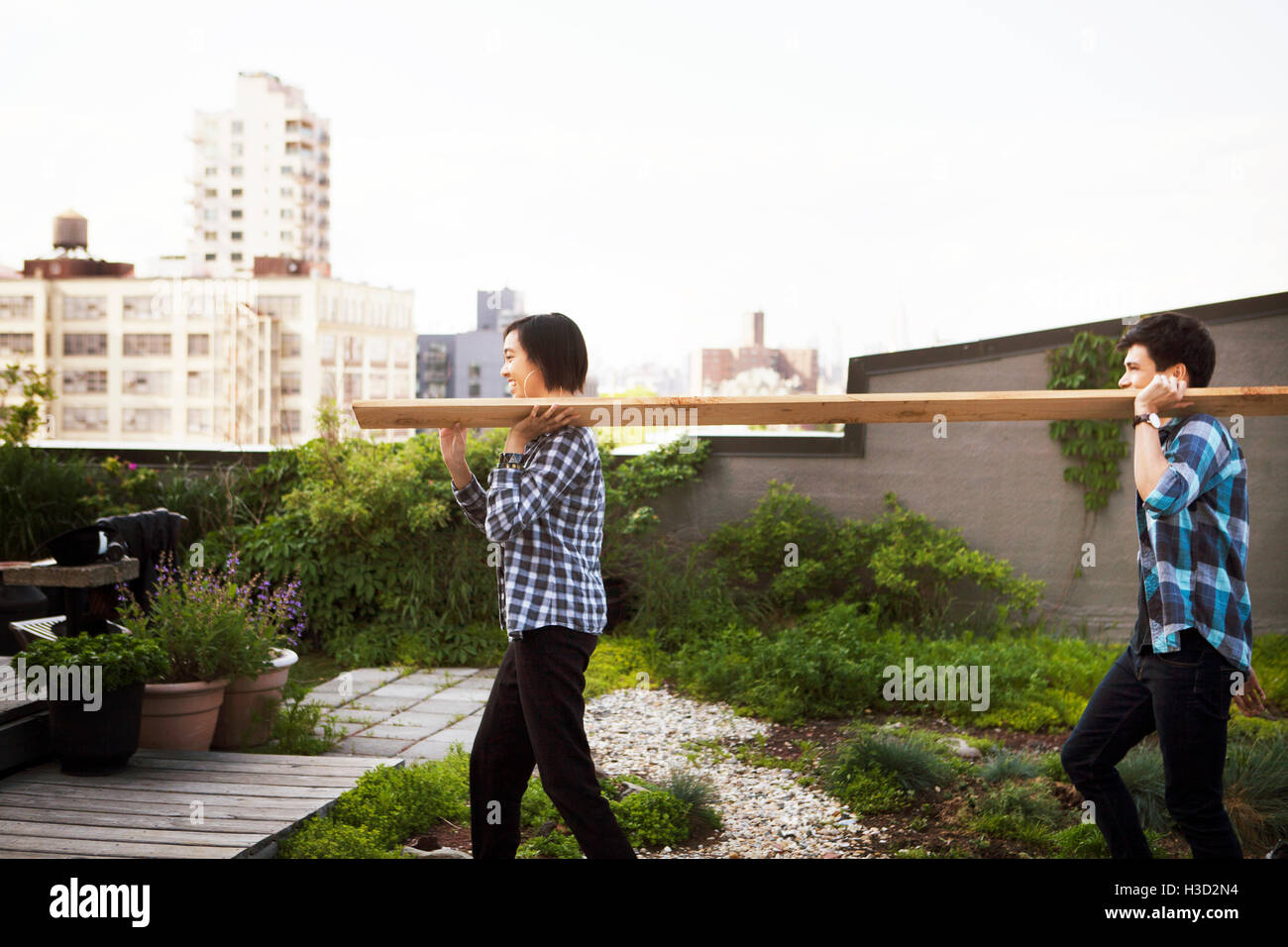 Side view of couple carrying wooden plank while walking on terrace Stock Photo