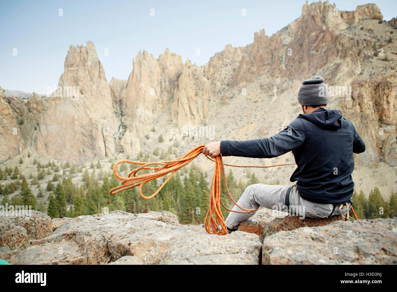 Rear view of rock climber throwing rope while siting on mountain Stock ...