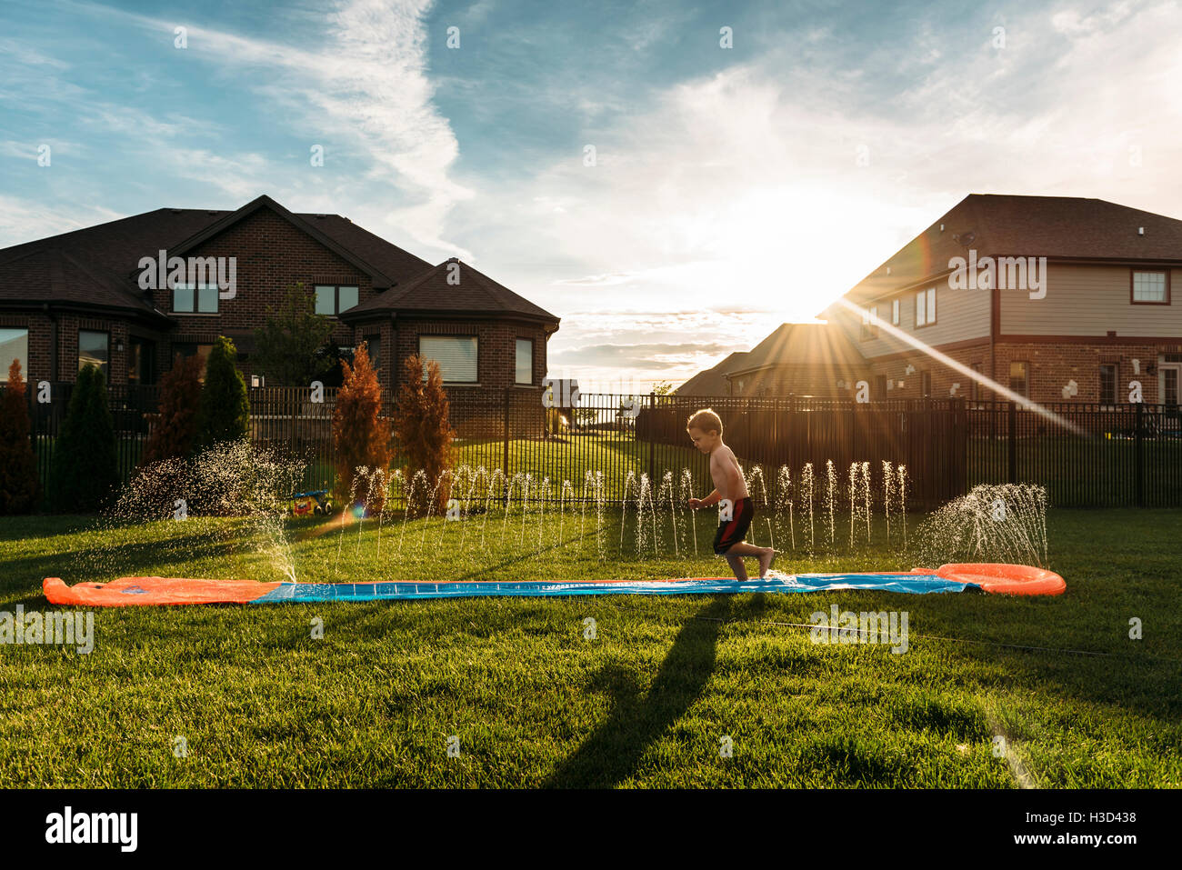 Boy jumping on water slide at backyard Stock Photo