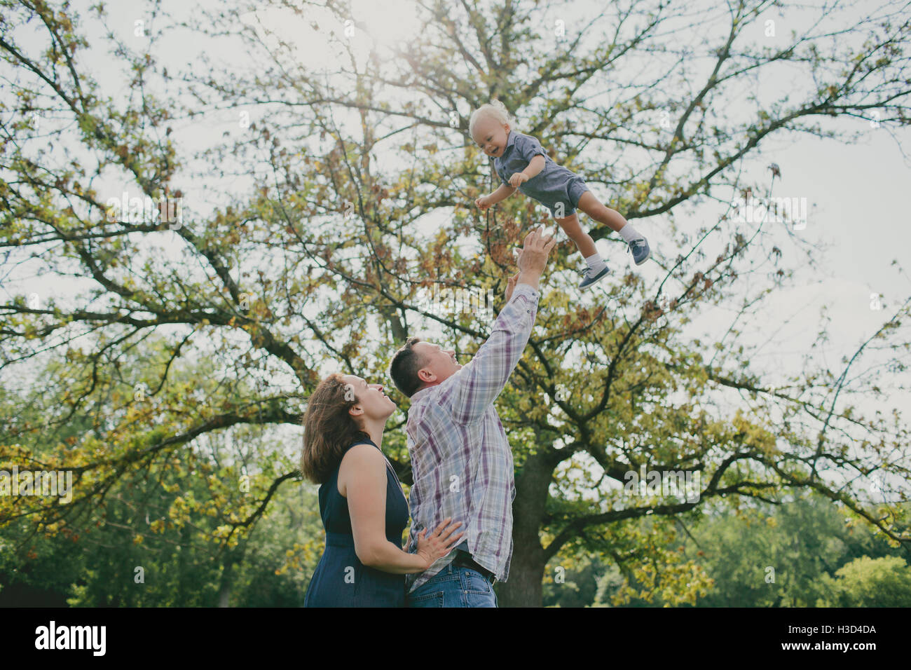 Cheerful man with wife throwing son in air Stock Photo