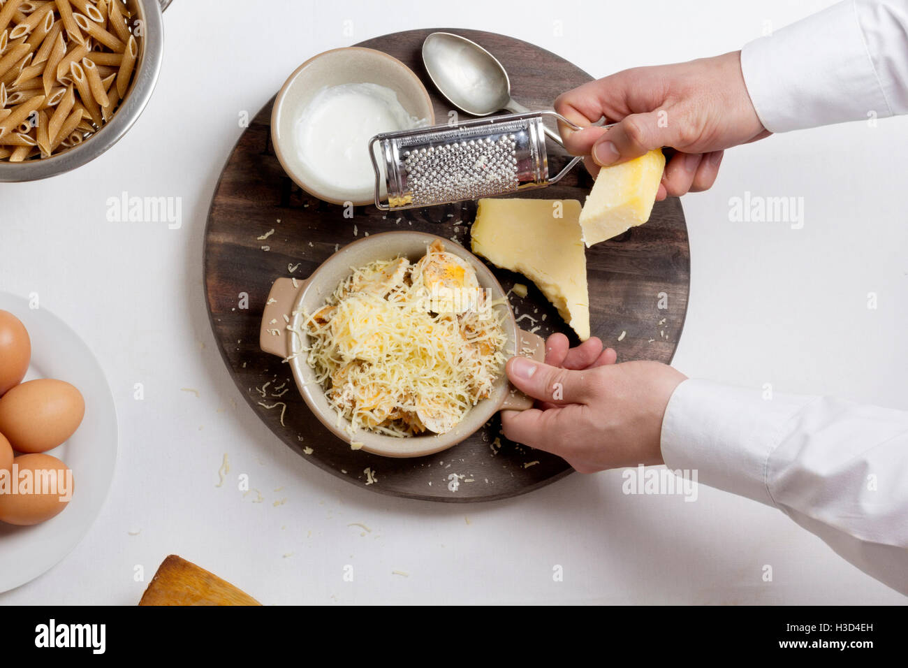 Overhead view of chef grating cheese on boiled eggs in bowl Stock Photo