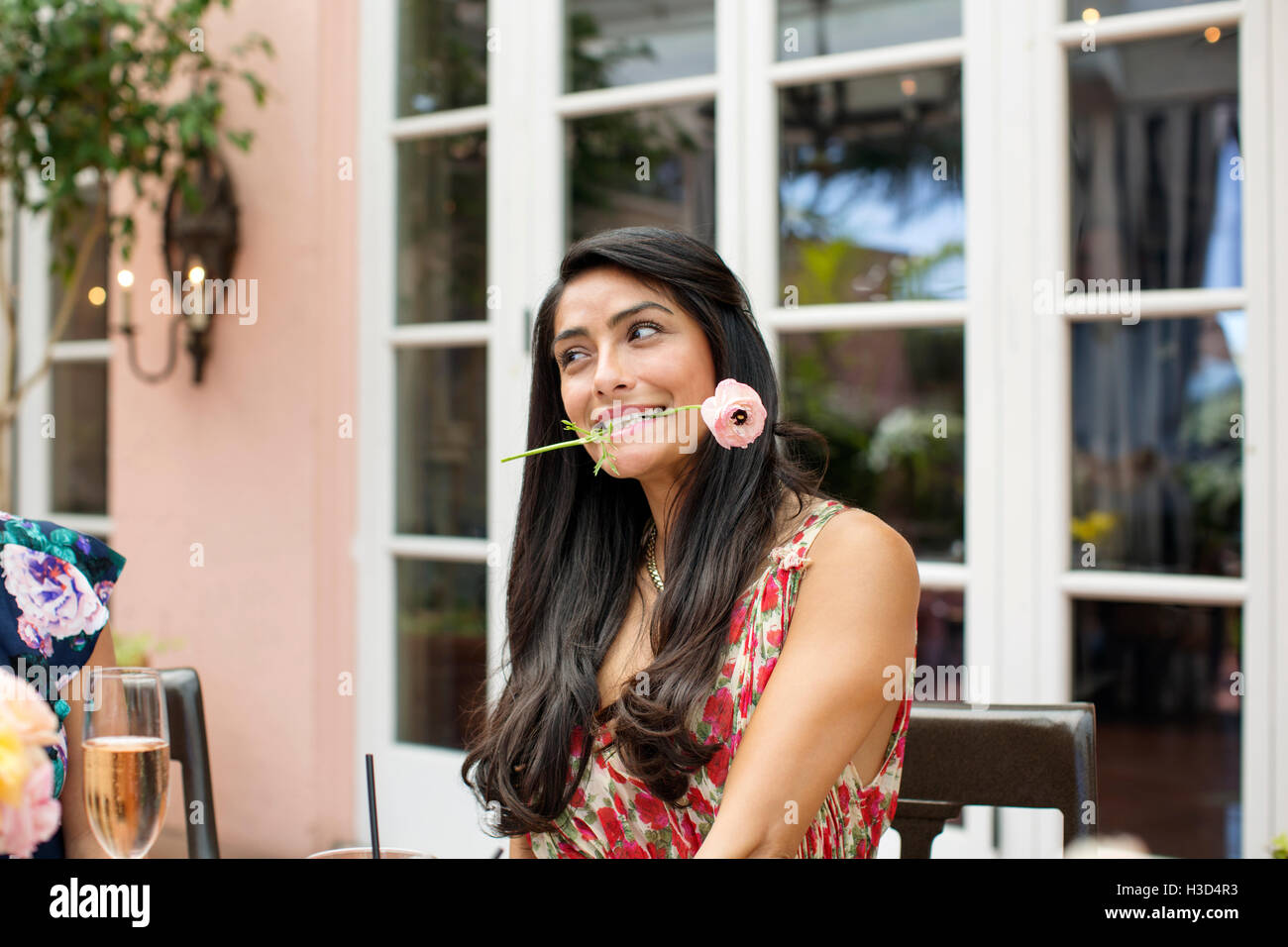 Beautiful woman holding flower in mouth at outdoor restaurant Stock Photo