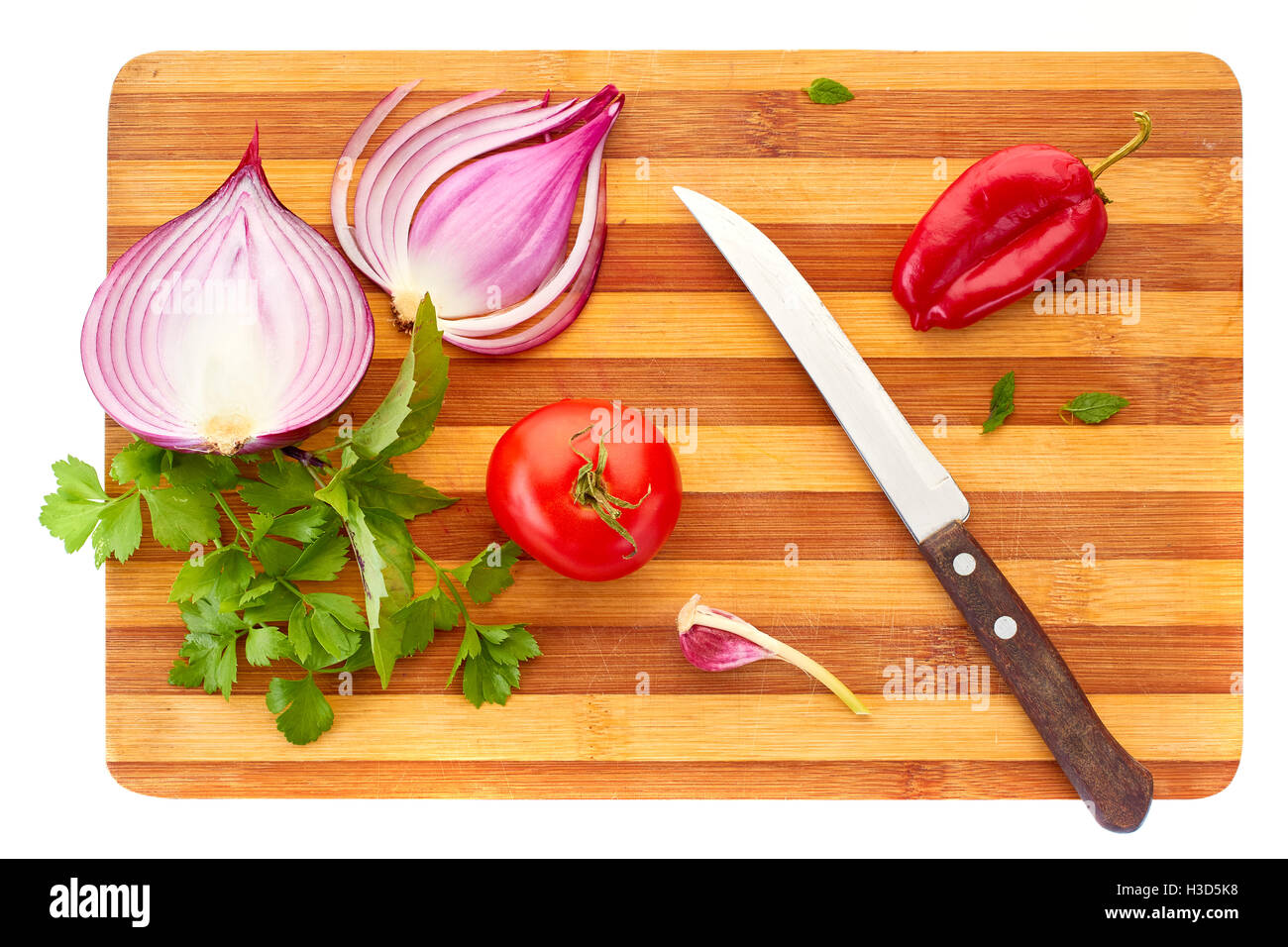 Sliced red onion, tomatoe,  pepper, garlic, basil and parsley with knife on wooden board over white background. Stock Photo