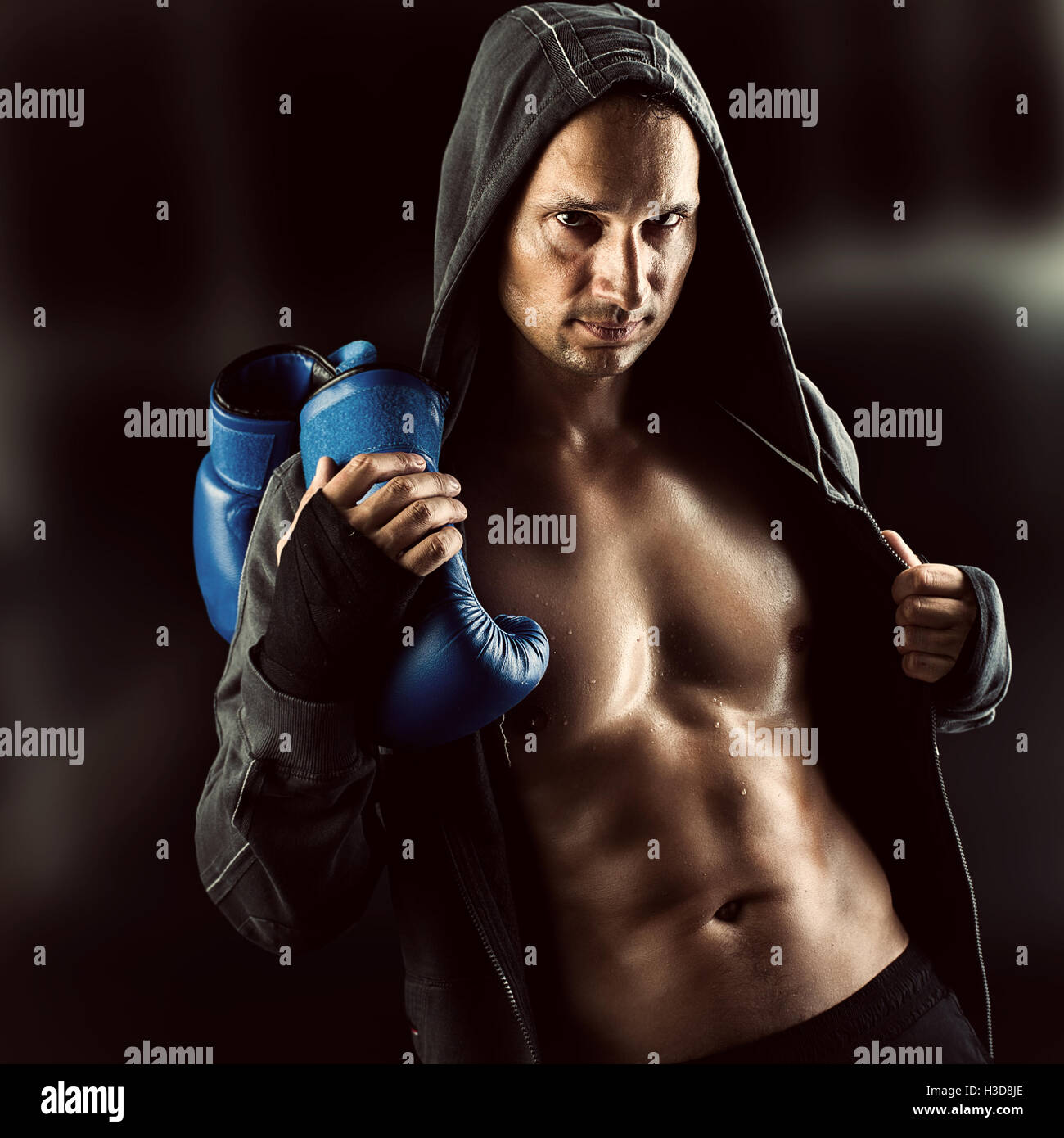 Serious Young muscular man boxer wearing jacket with hood. Boxing gloves  slung over his shoulder on dark background indoor Stock Photo - Alamy