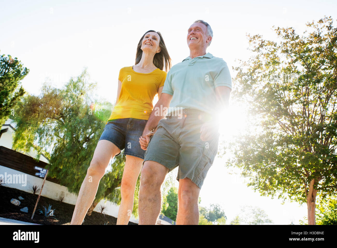Senior couple wearing shorts walking along a street in the sunshine. Stock Photo