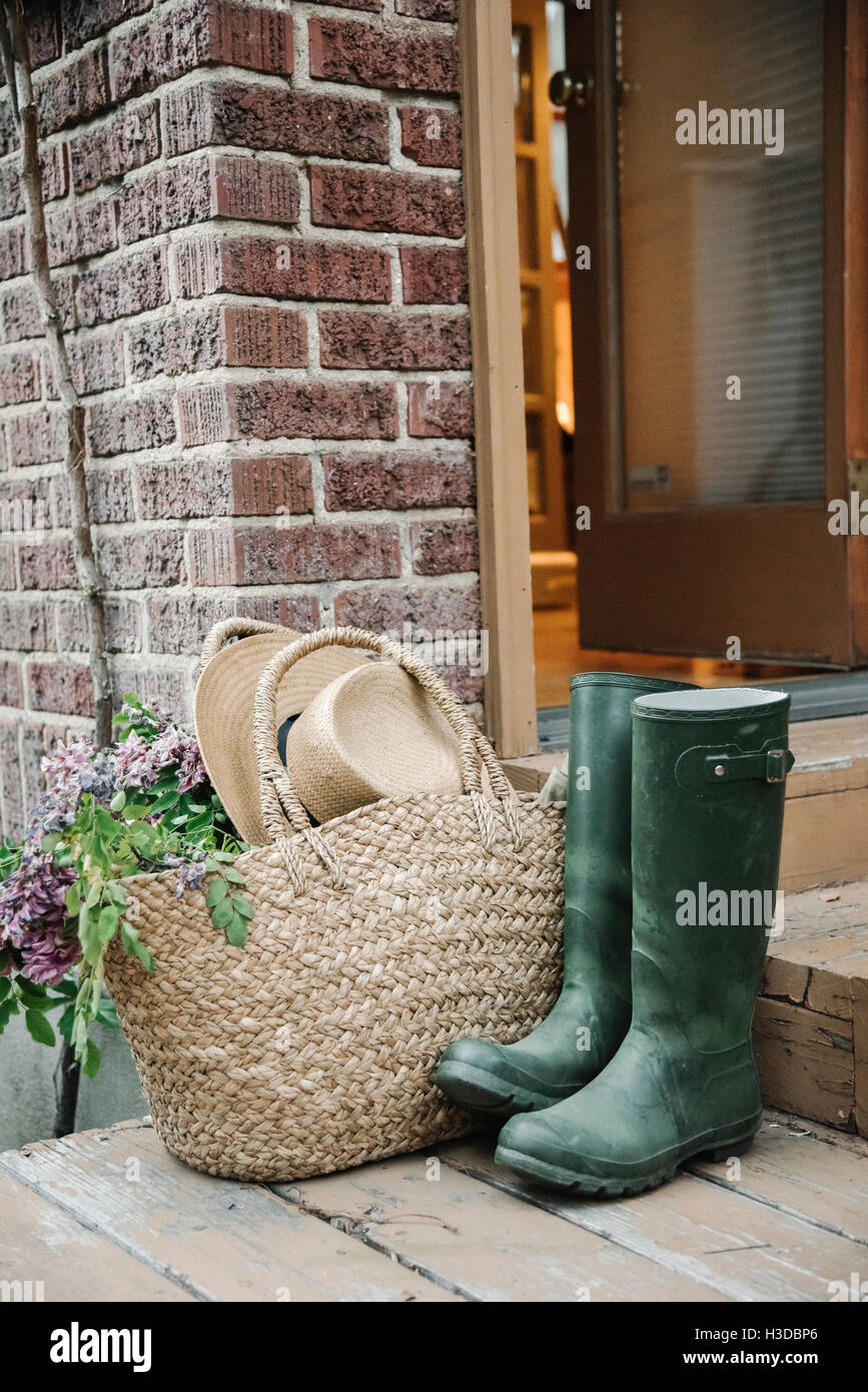 Wellingtons, rubber boots, basket and straw hat by a doorway. Stock Photo