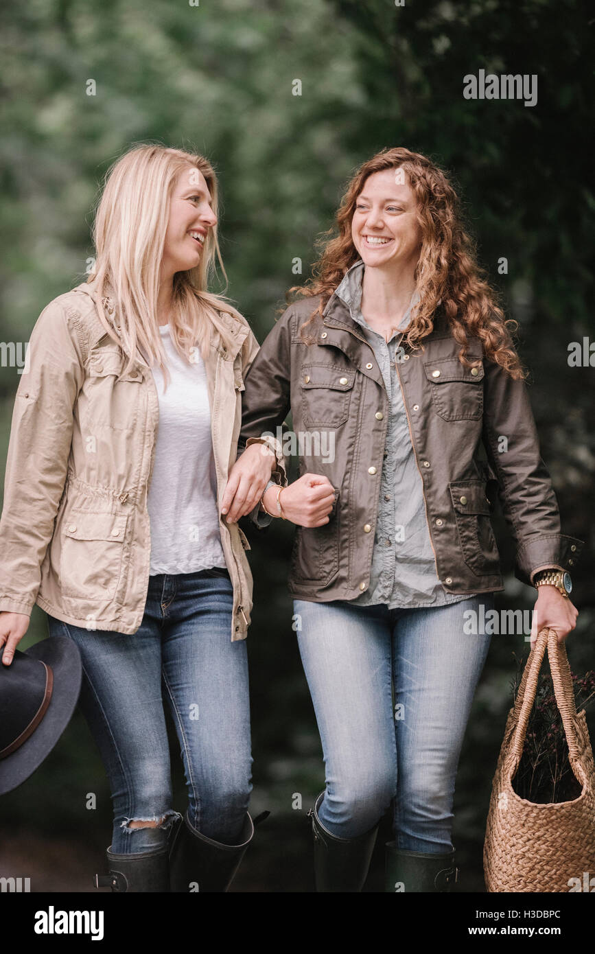 Two women arm in arm walking in coats and boots along a country path with a basket. Stock Photo