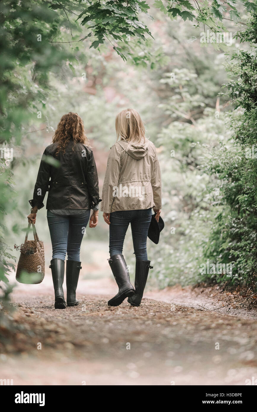 Two women walking in coats and boots along a country path with a basket. Stock Photo