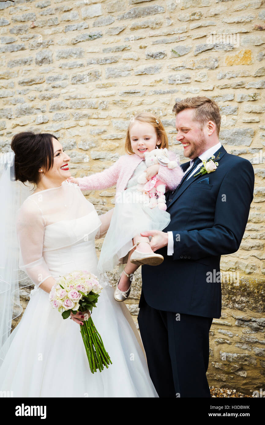 A bride and groom, a couple on their wedding day, holding a young child. Stock Photo