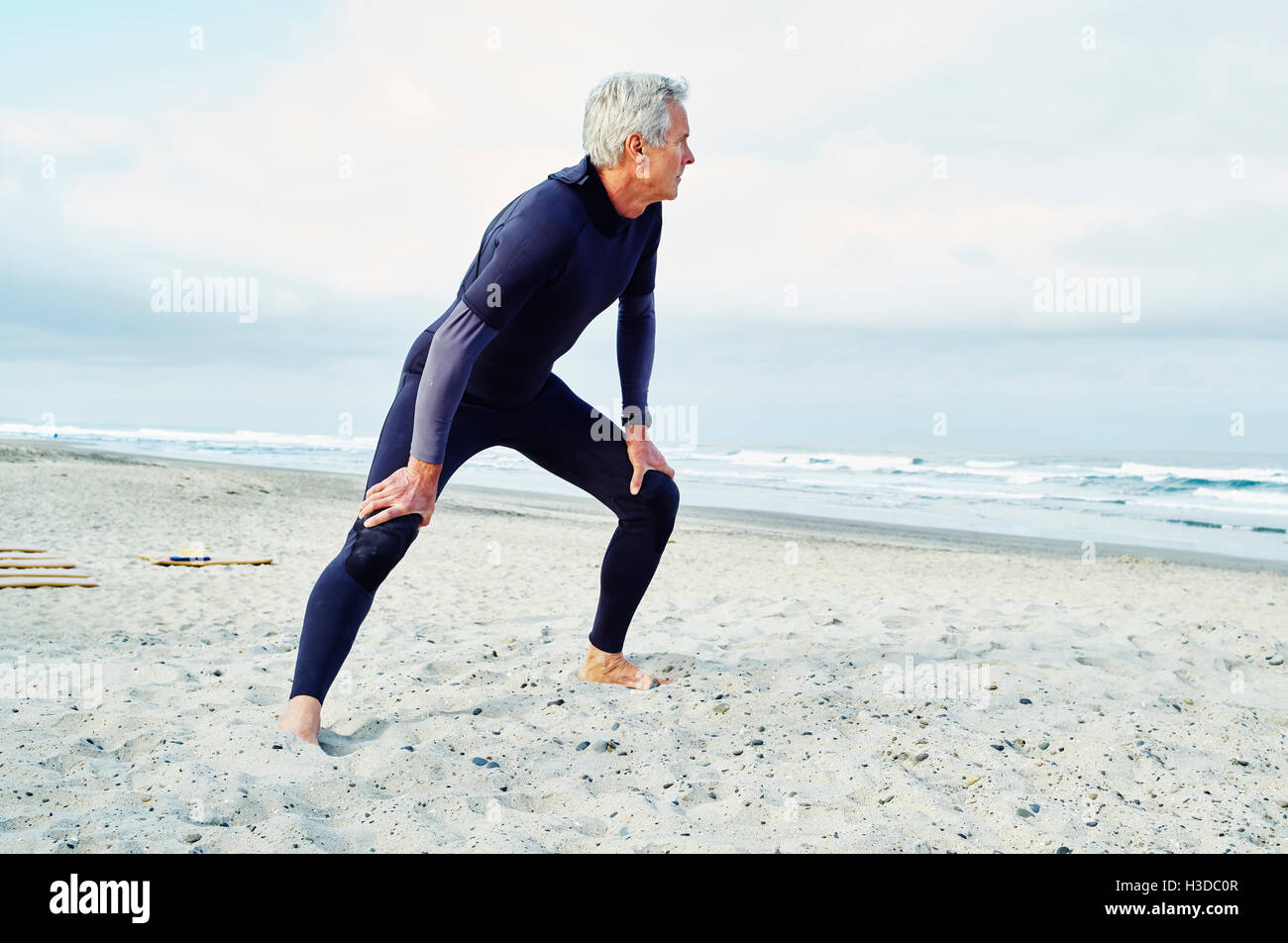 Senior man wearing wetsuit standing on a sandy beach. Stock Photo