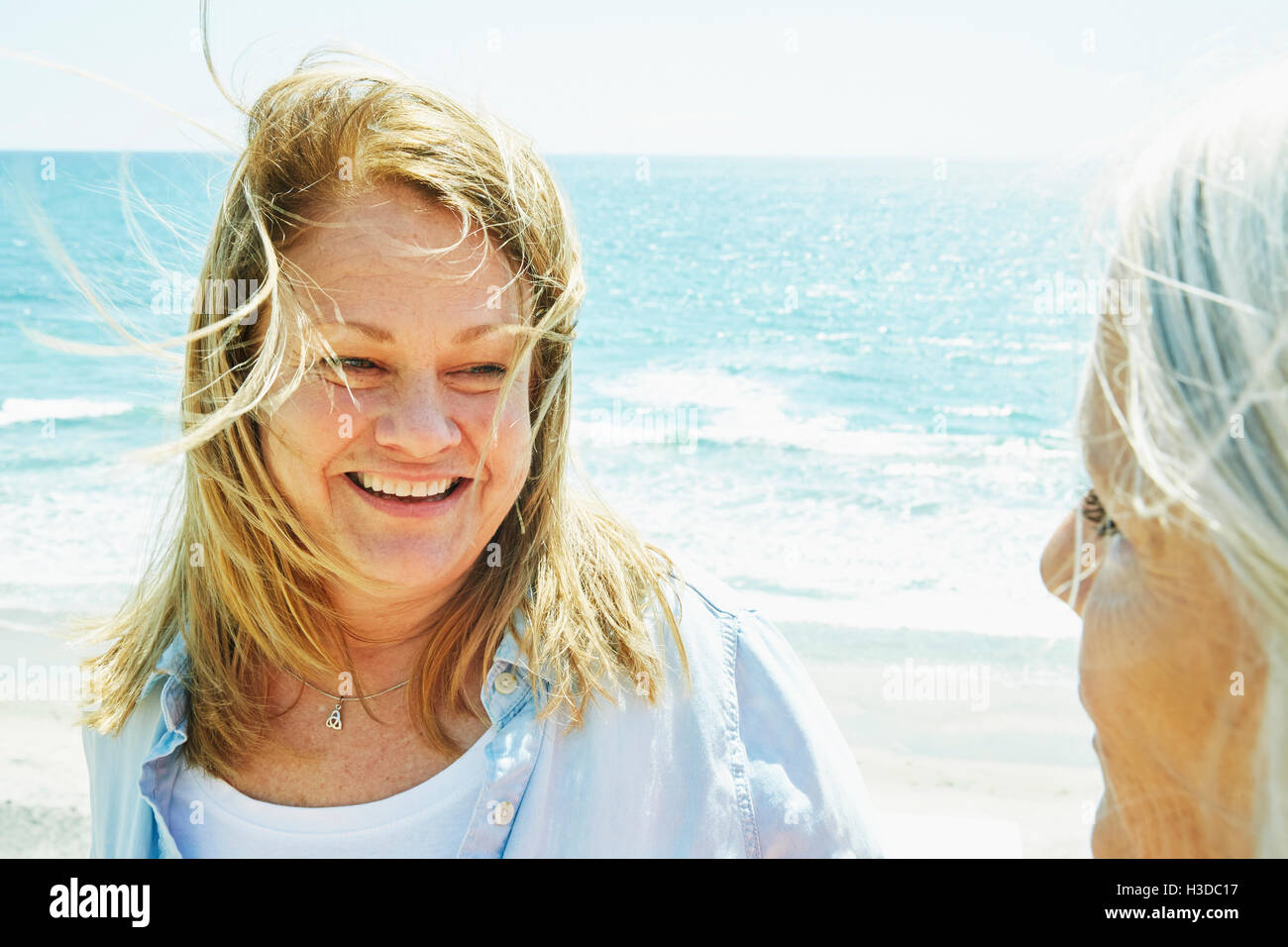 Smiling blond mature women standing by the ocean. Stock Photo