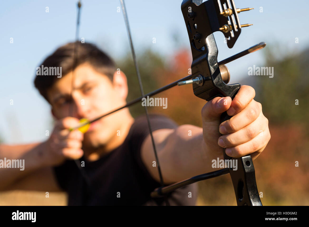 An archer drawing his compound bow in a field in the forest during the early autumn. Stock Photo