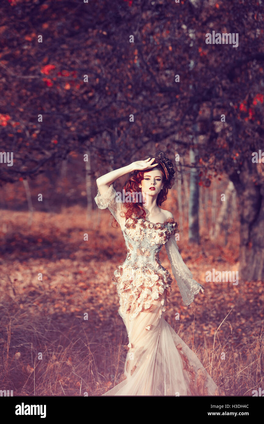Red hair girl in beautyful fasion dress standing at the yellowed tree Stock Photo