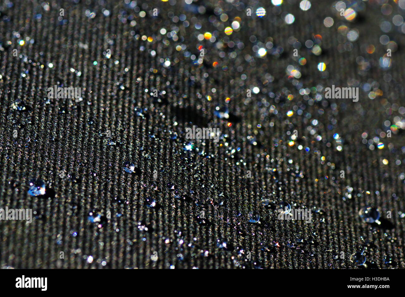 Drops of water on a black impregnated material in the light of the sun. Stock Photo