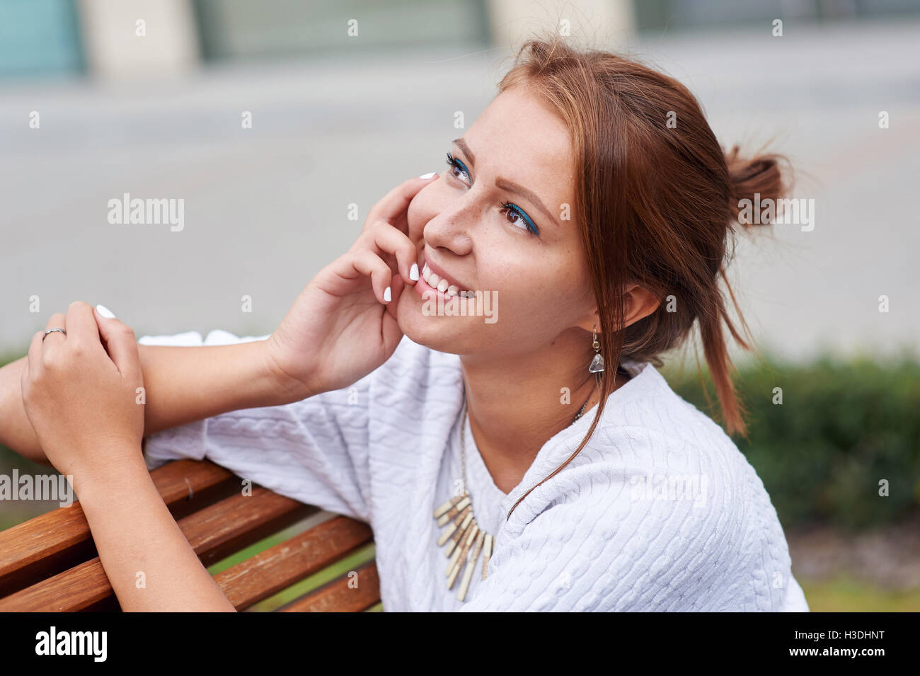 Beautiful young woman sits on a bench in the summer park Stock Photo
