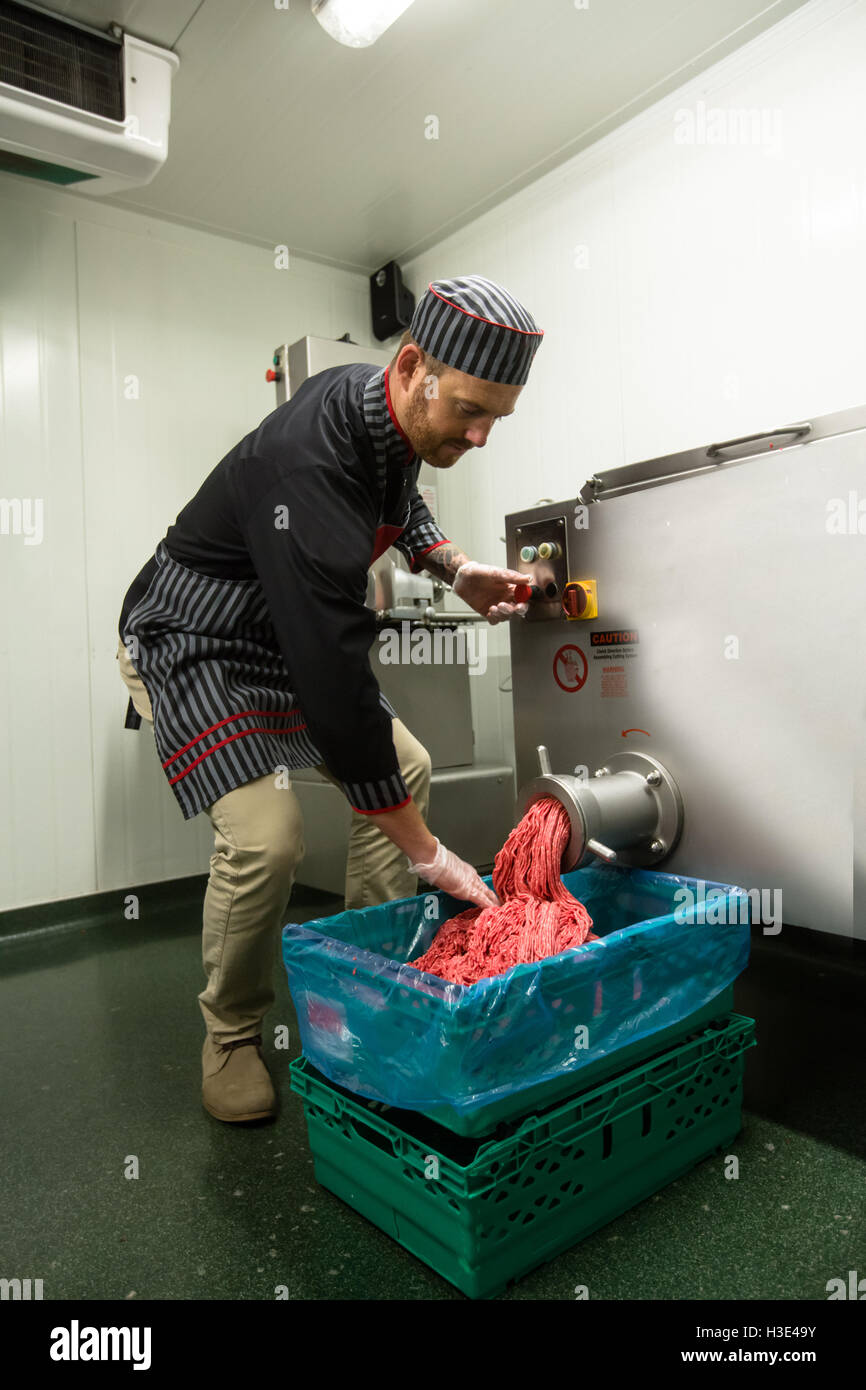 Butcher looking at minced meat coming out from grinder at butchers shop