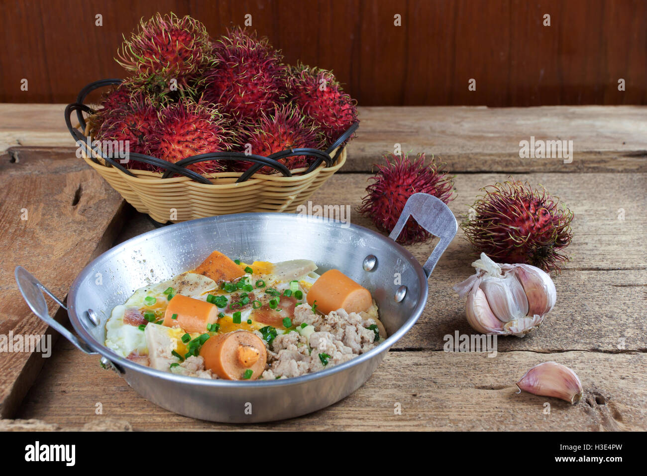 Indochina pan-fried egg with pork and sausage toppings on wood table. Rambutan fruit. Stock Photo