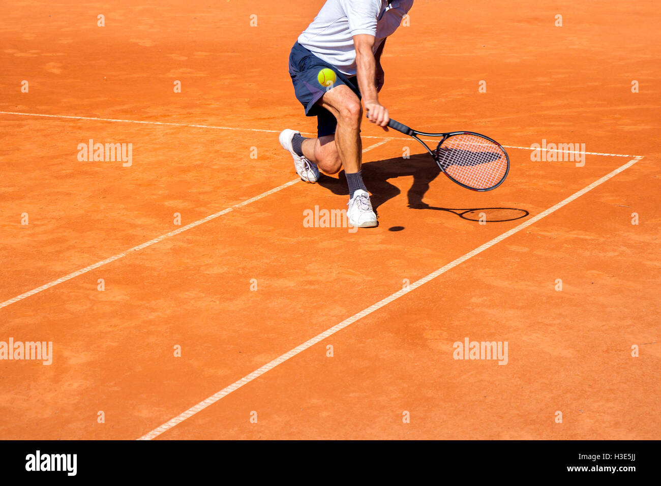 Male tennis player in action on the clay court on a sunny day Stock Photo
