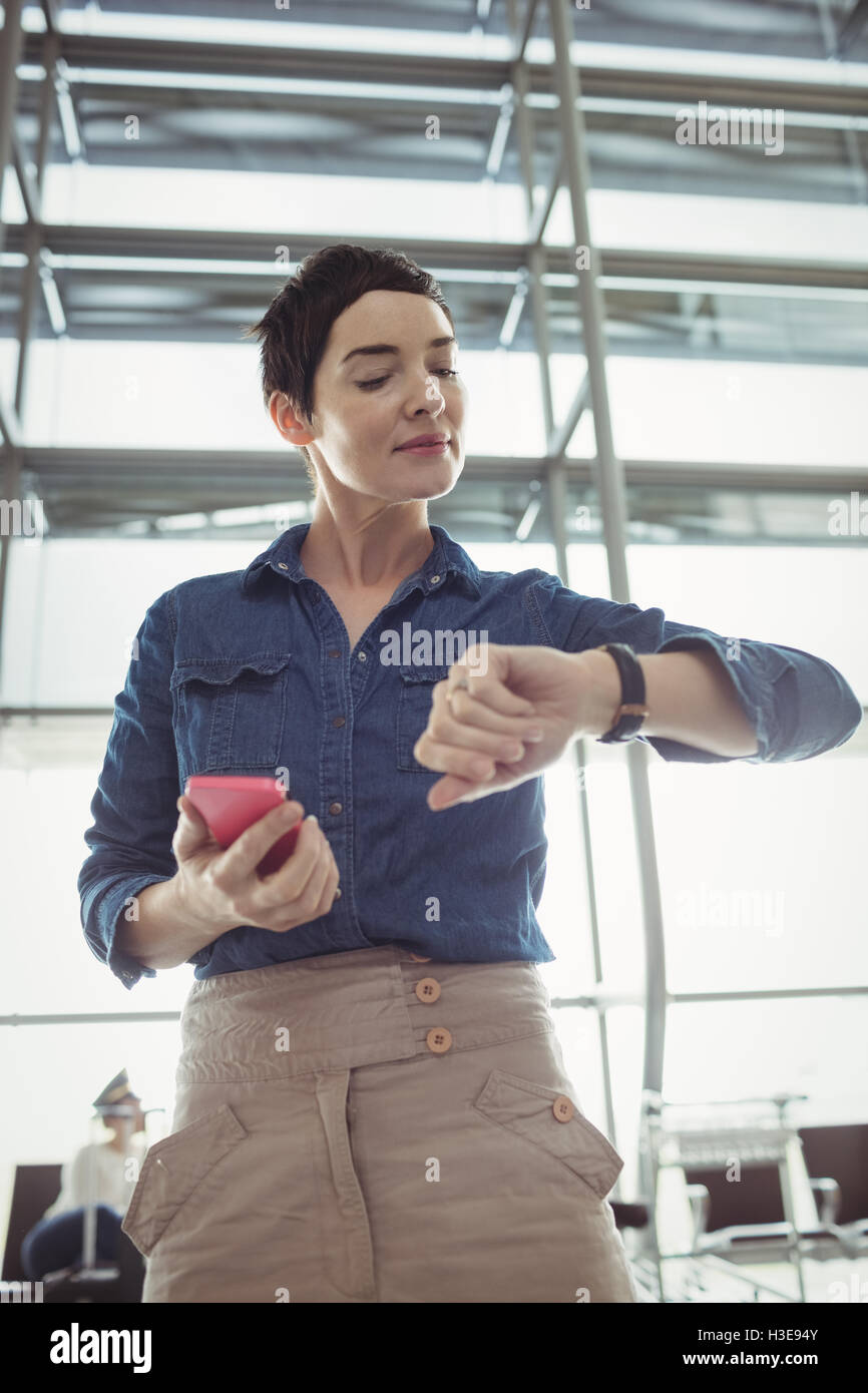 Businesswoman checking time while using mobile phone Stock Photo