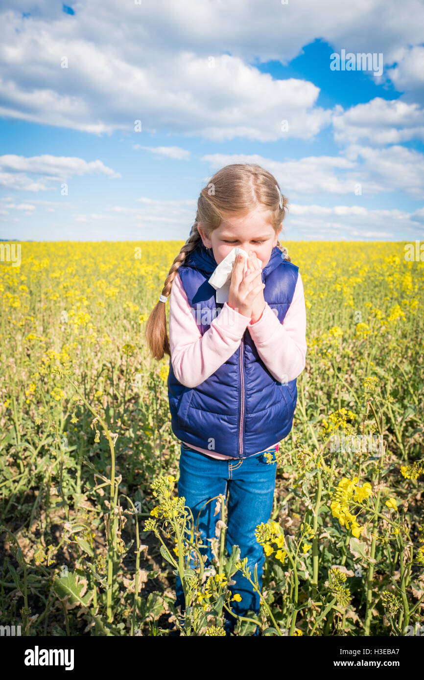 Little girl outside sneezing and not feeling well blowing her nose and suffering from pollen allergy. Stock Photo