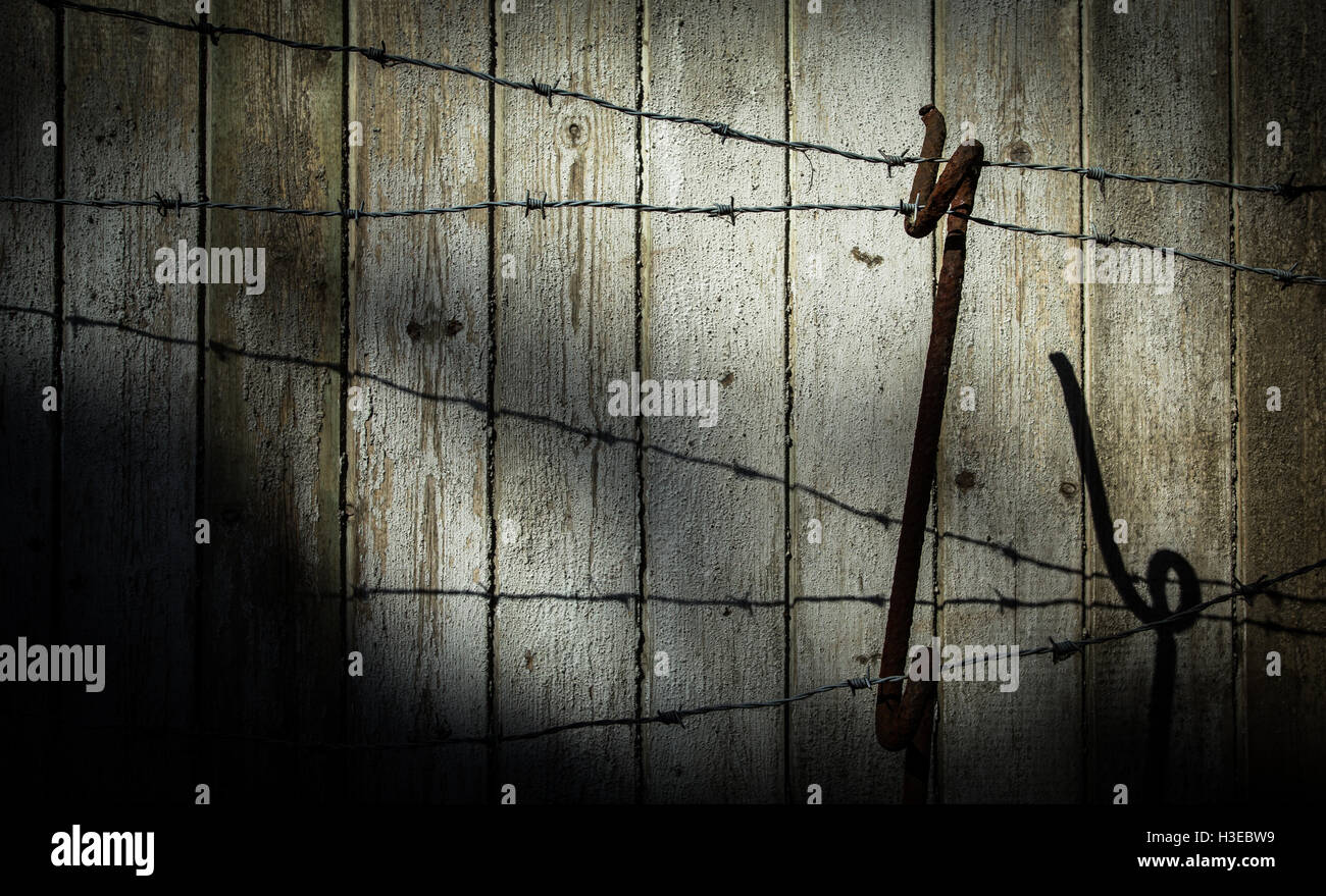 Strands of a barbed wire fence and support from WWI days against the faded planks of an old wooden fence with ominous shadows Stock Photo