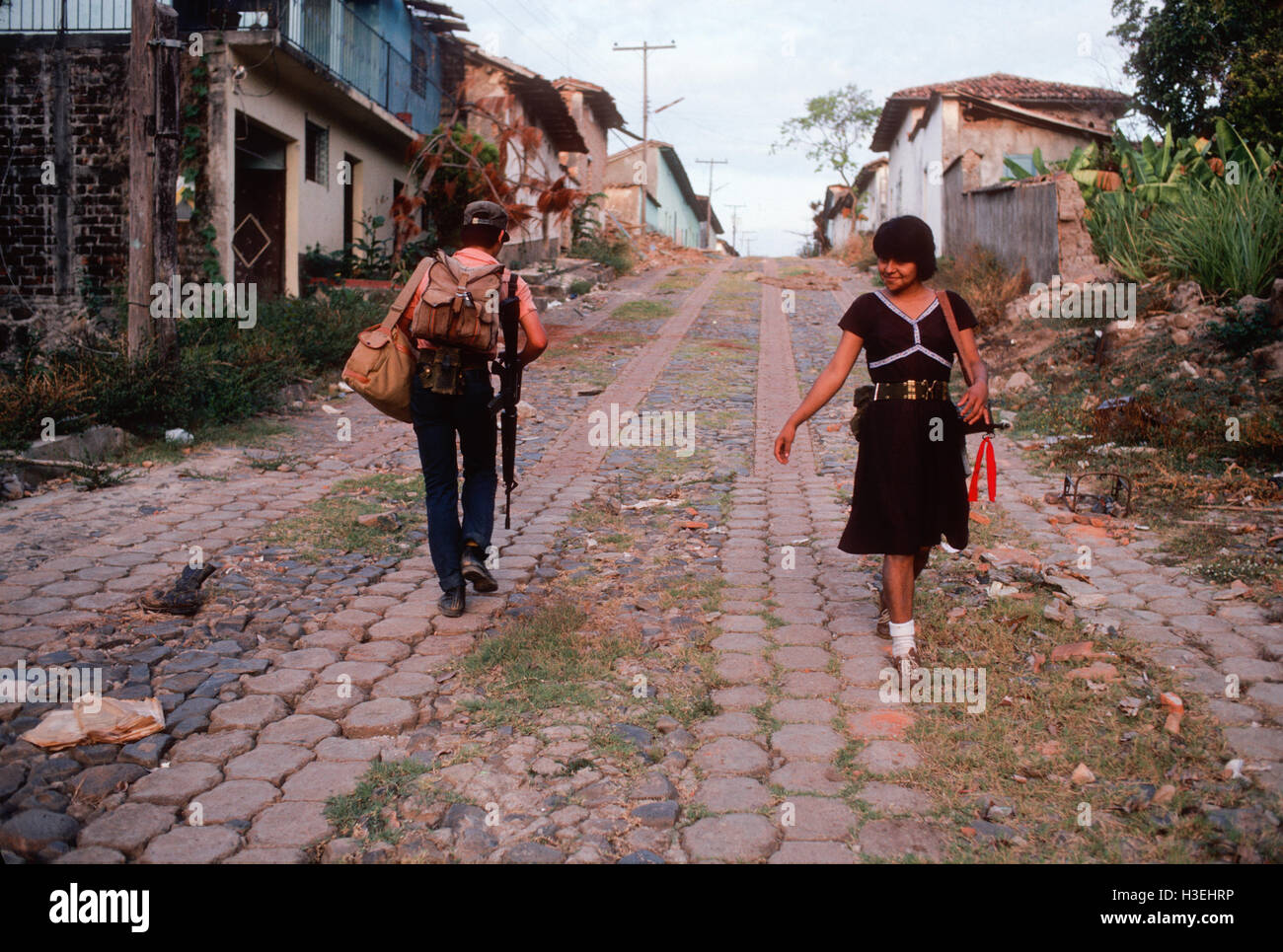TENANCINGO,  EL SALVADOR, MARCH 1984: - Within the FPL Guerrilla's Zones of Control.  A teenage woman guerrilla fighter smiles at a friend as she passes him in the ruined street of Tenancingo. Stock Photo