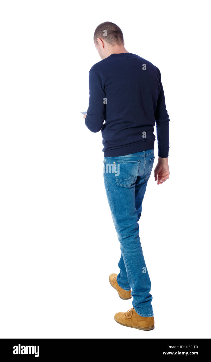 back view of a man walking with a mobile phone. back view of man in motion. backside view of person. Rear view people collection. Isolated over white background. The guy in the black sweater is looking at the phone. Stock Photo